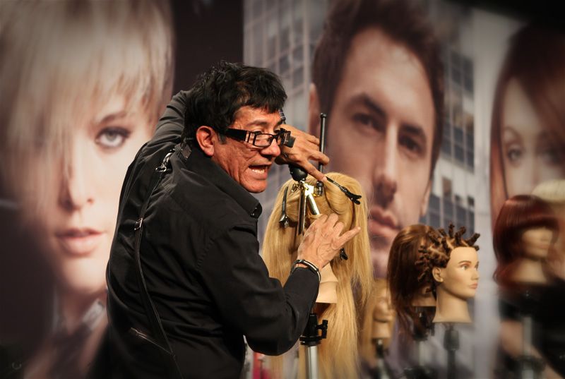 Sam Villa cutting a blonde mannequin's hair at an education event.