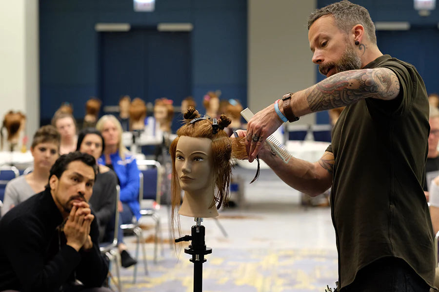 Culture Ambassador for Sam Villa Andrew Caruthers demonstrating a haircut on a mannequin in front of a group of students.