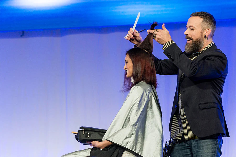 Sam Villa artist Andrew Carruthers demonstrating a haircut on a brunette model on a stage. 