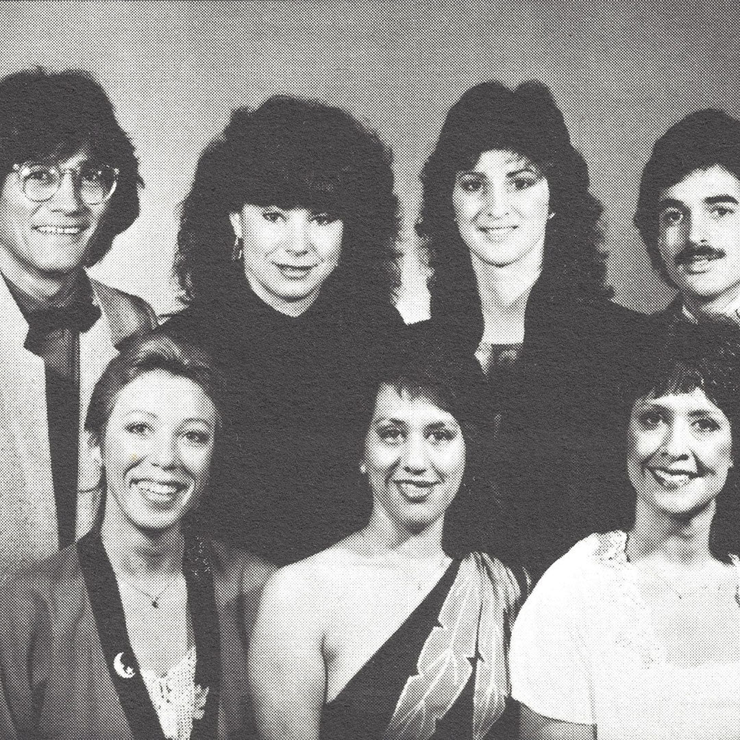 A vintage black-and-white group portrait of seven smiling individuals, featuring a mix of men and women in both formal and casual attire, with a retro halftone effect.