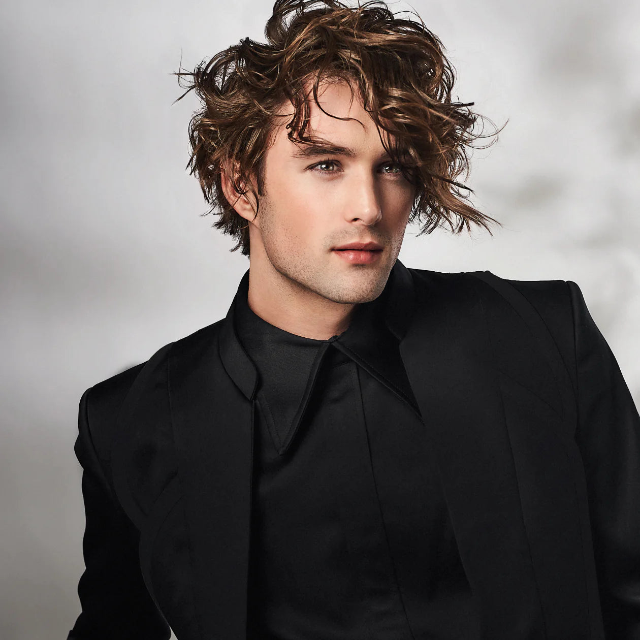 Male Model with Brunette Curly Hair in a Black Blazer and Black Shirt